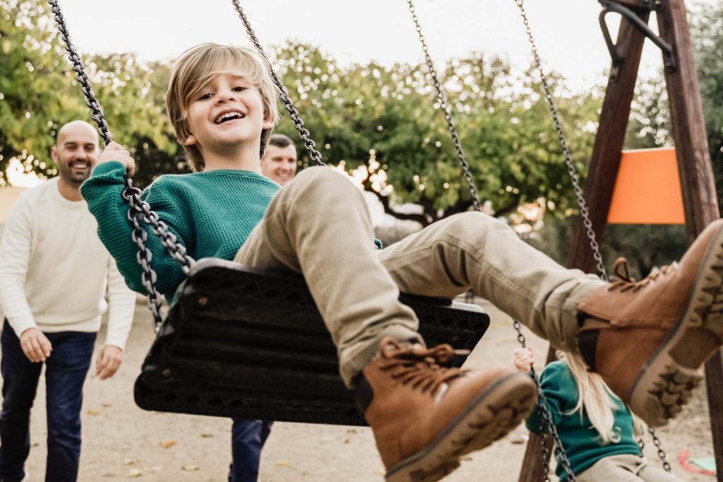 LGBT family - Happy children sons and fathers having fun swinging on swing at city park